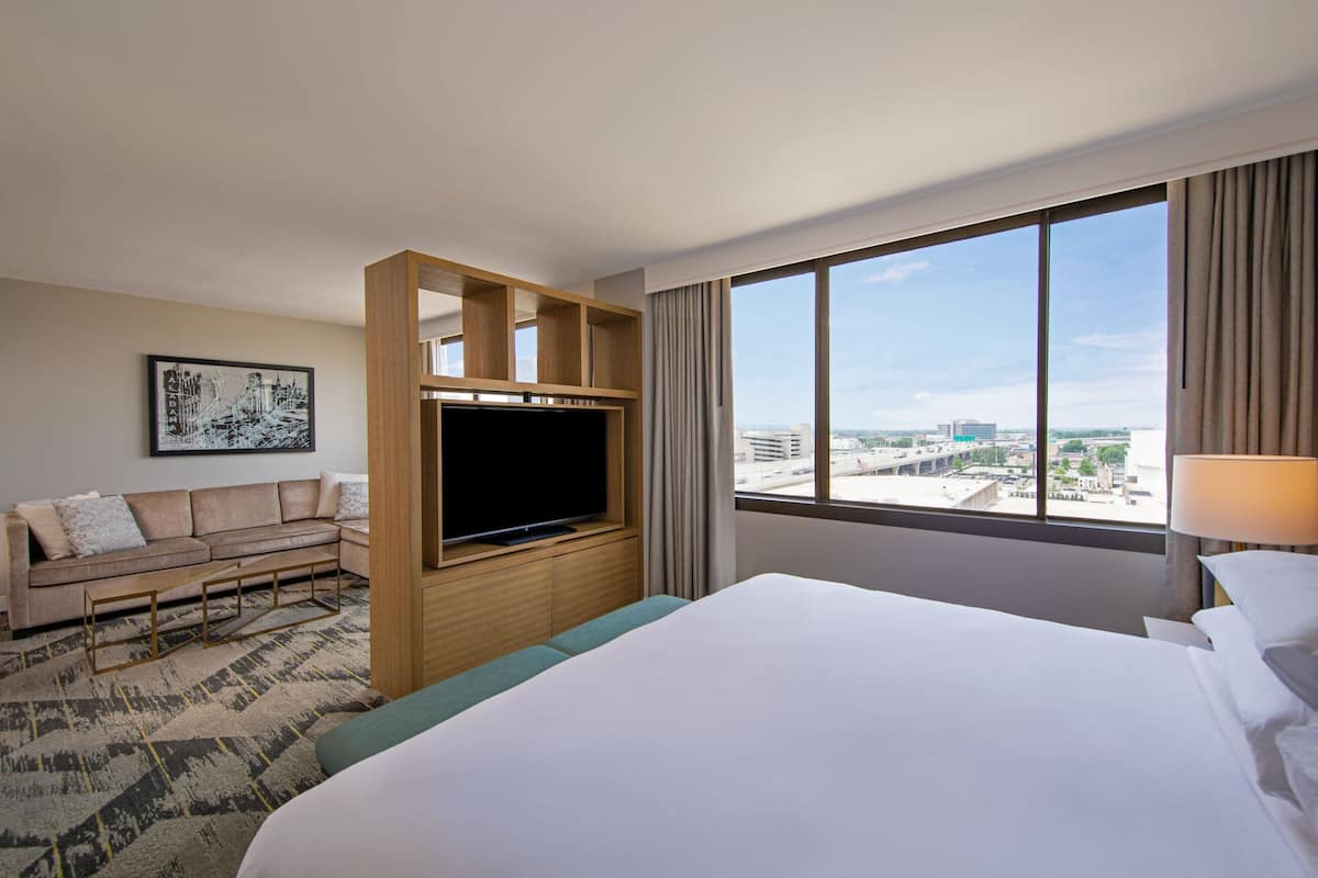 A hotel room with a large bed, a sofa, a TV, and a city view.