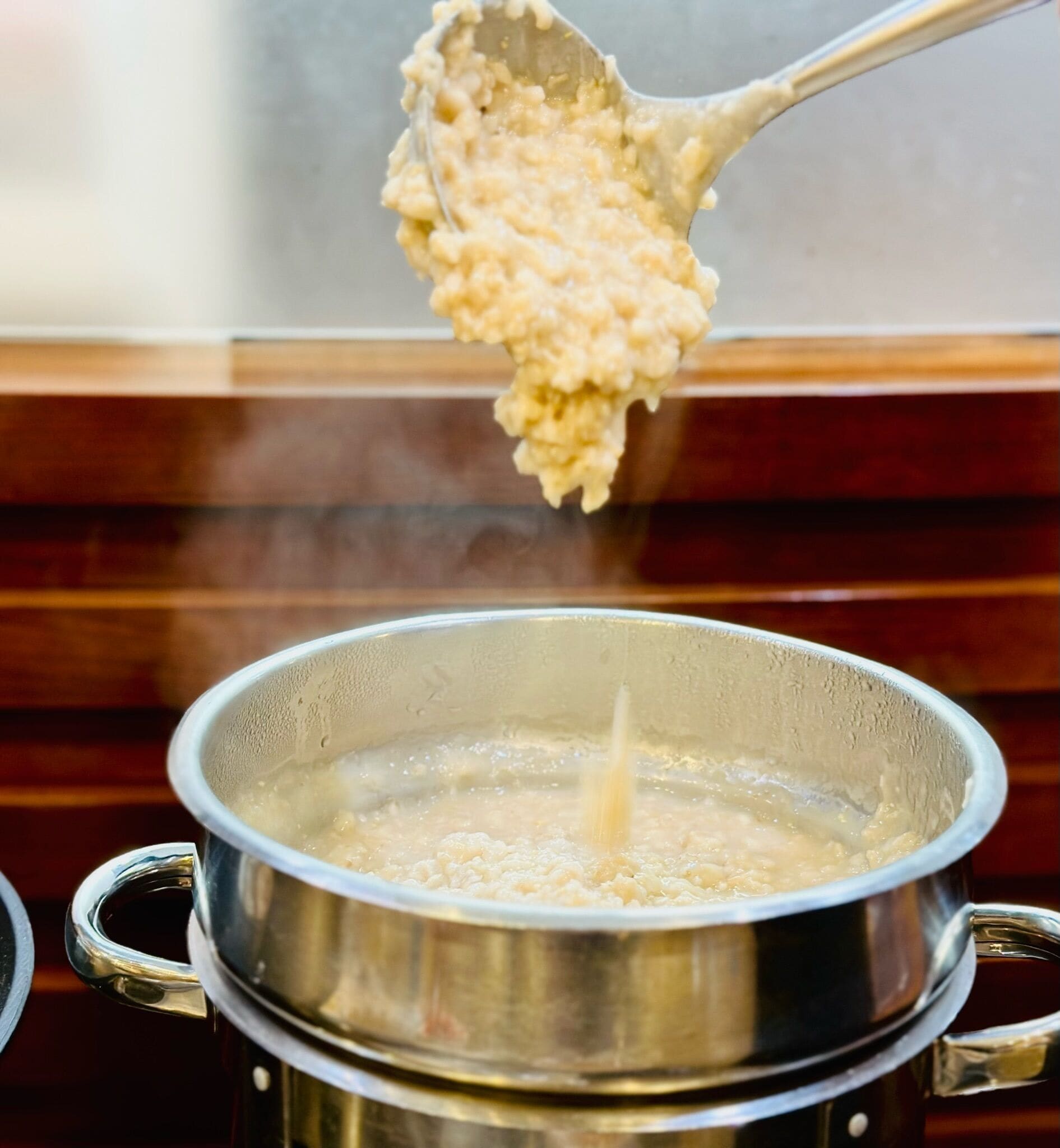 Gros plan d’une marmite dans laquelle une louche soulève une substance crémeuse, probablement une soupe ou une bouillie, et de laquelle s’échappe de la vapeur.