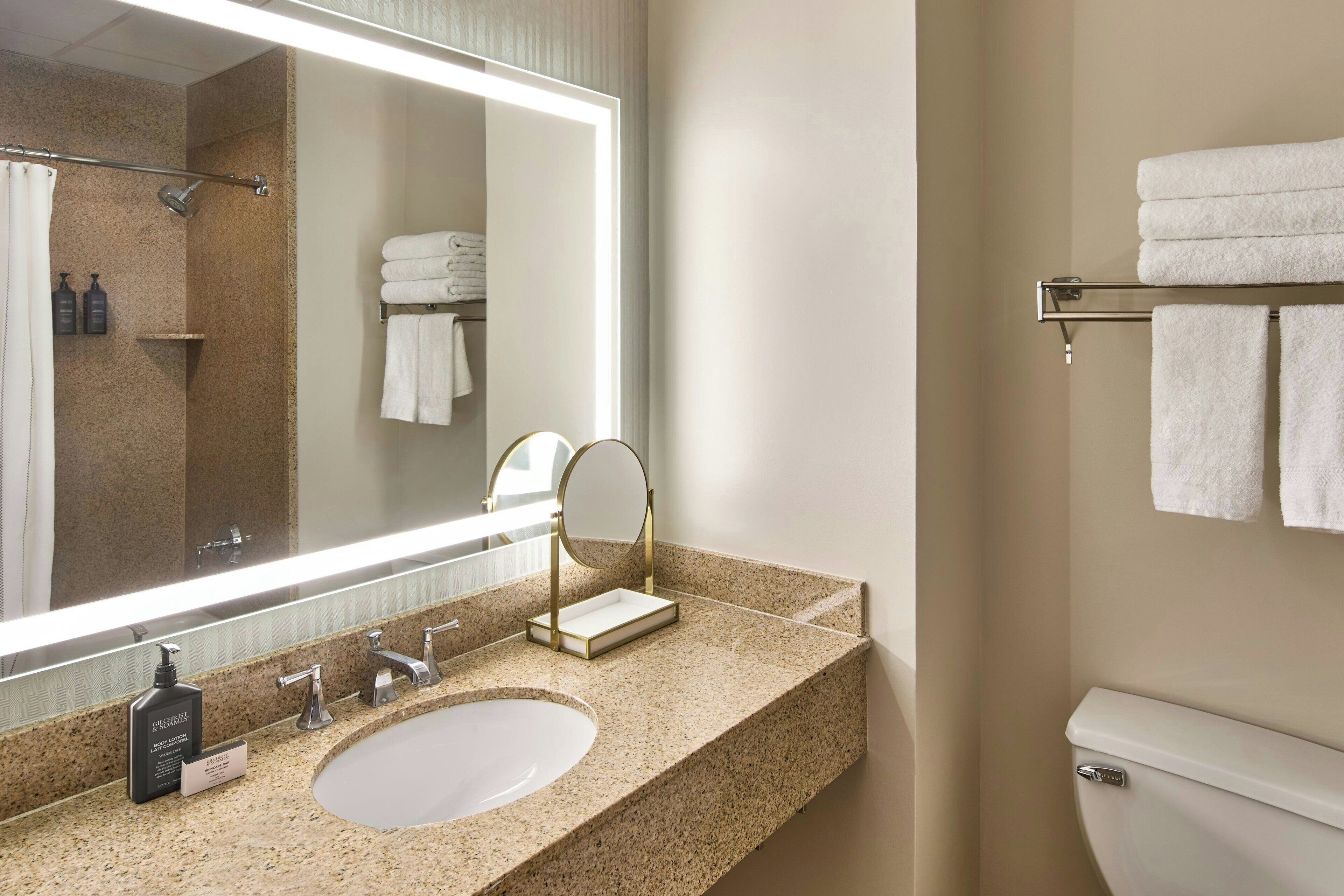 A bathroom with a granite countertop, a sink, a mirror, a towel rack, and a toilet.