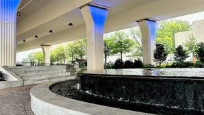 A covered outdoor area with a central water feature, stone steps, and columns with blue lighting. - Sheraton Birmingham Hotel (Birmingham)