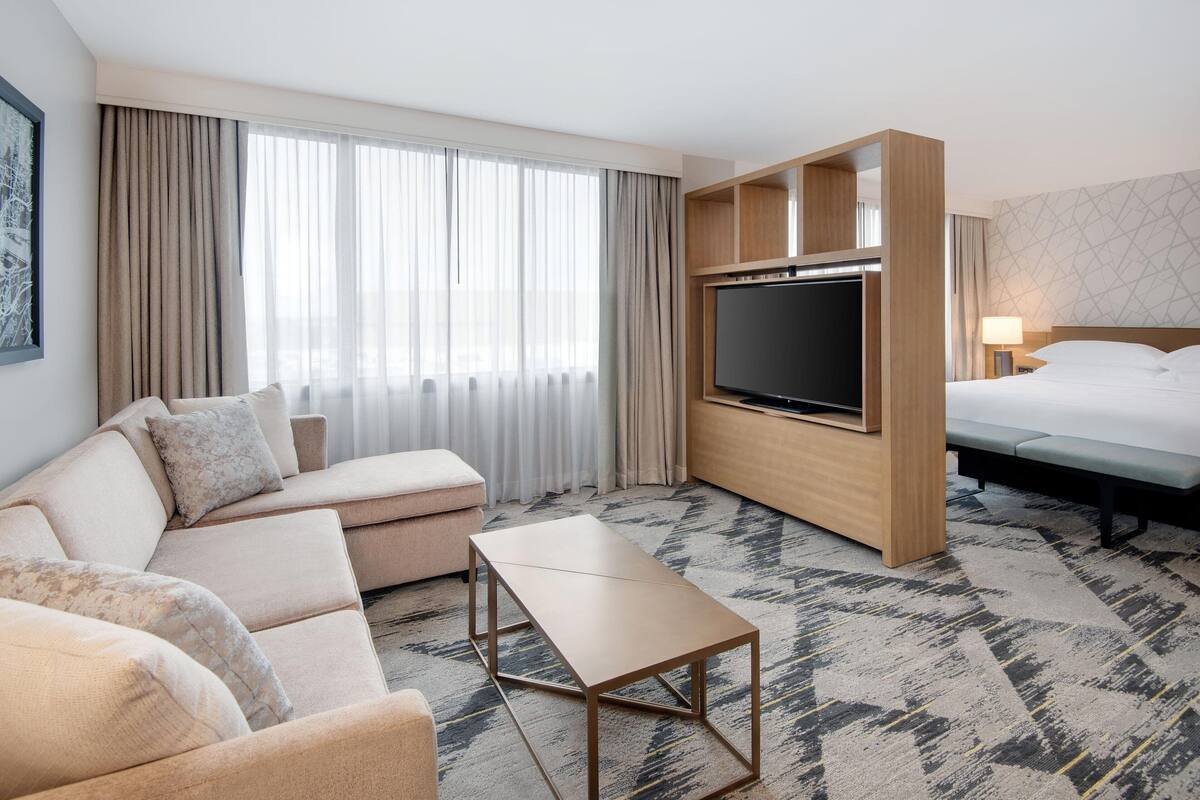 A modern hotel room with a sofa, a TV, a bed, and a small table.