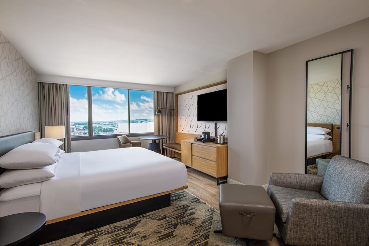 A hotel room with a large bed, a desk, a sofa, a TV, and a view of the city.