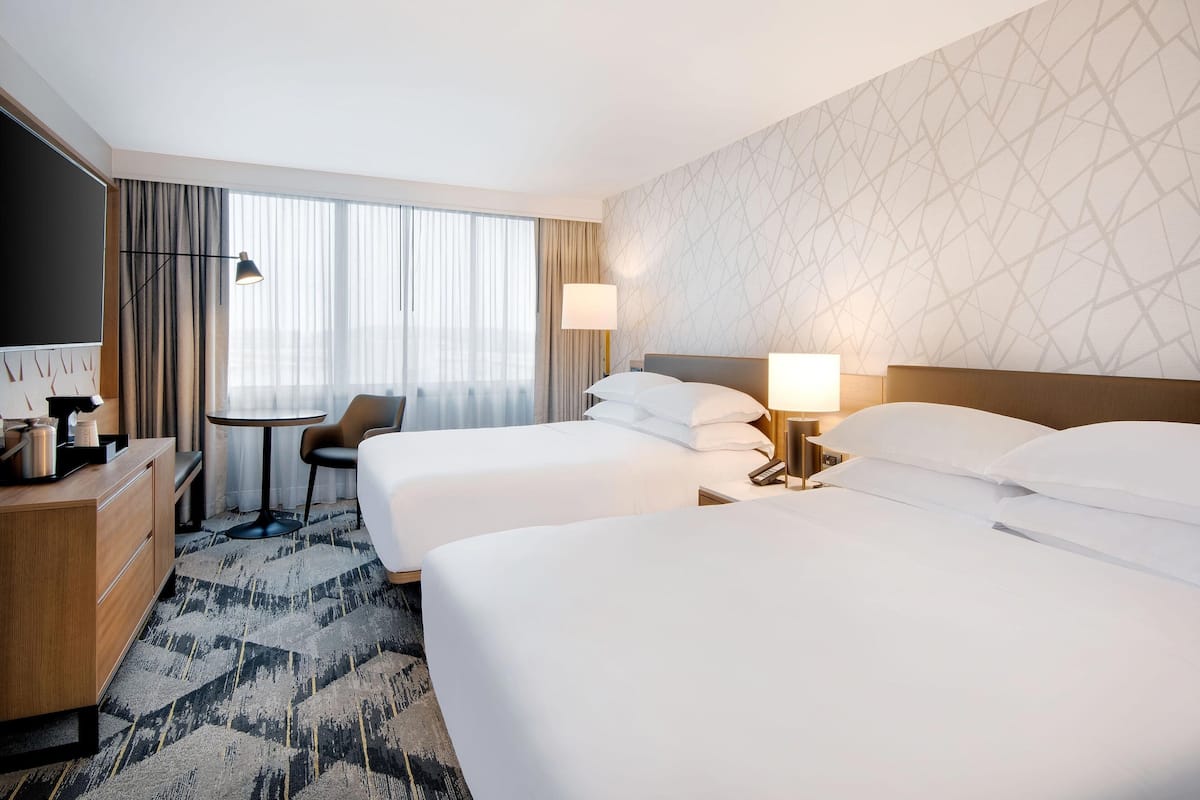 A hotel room with two beds, a desk, a chair, a TV, and a window with curtains.