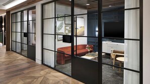 A modern hotel room with a wooden floor, a red sofa, a small table with a vase, and a TV on the wall. - Sheraton Birmingham Hotel (Birmingham)