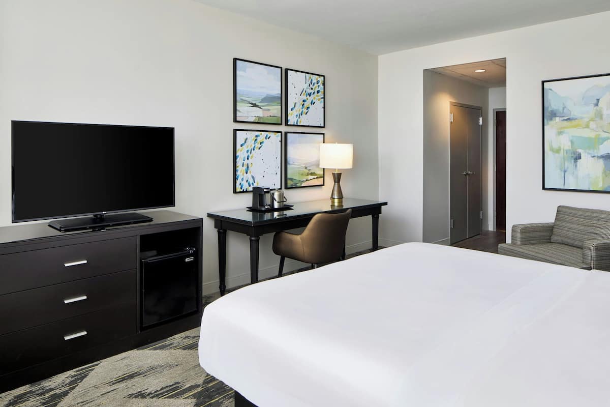 A hotel room with a bed, a desk with a chair, a television, and artwork on the walls.