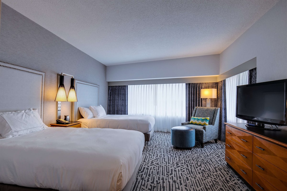 A hotel room with two beds, a television, a desk with a lamp, and a patterned rug.