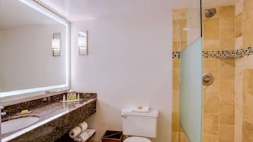 Un baño con lavamanos de mármol, inodoro, cabina de ducha de vidrio y espejo con apliques de pared.