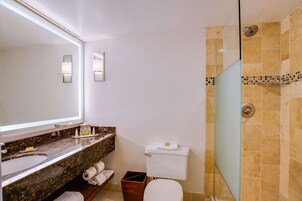 Un baño con lavamanos de mármol, inodoro, cabina de ducha de vidrio y espejo con apliques de pared.
