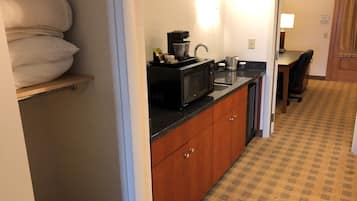 A compact kitchen with wooden cabinets, a microwave, a coffee maker, and a sink.