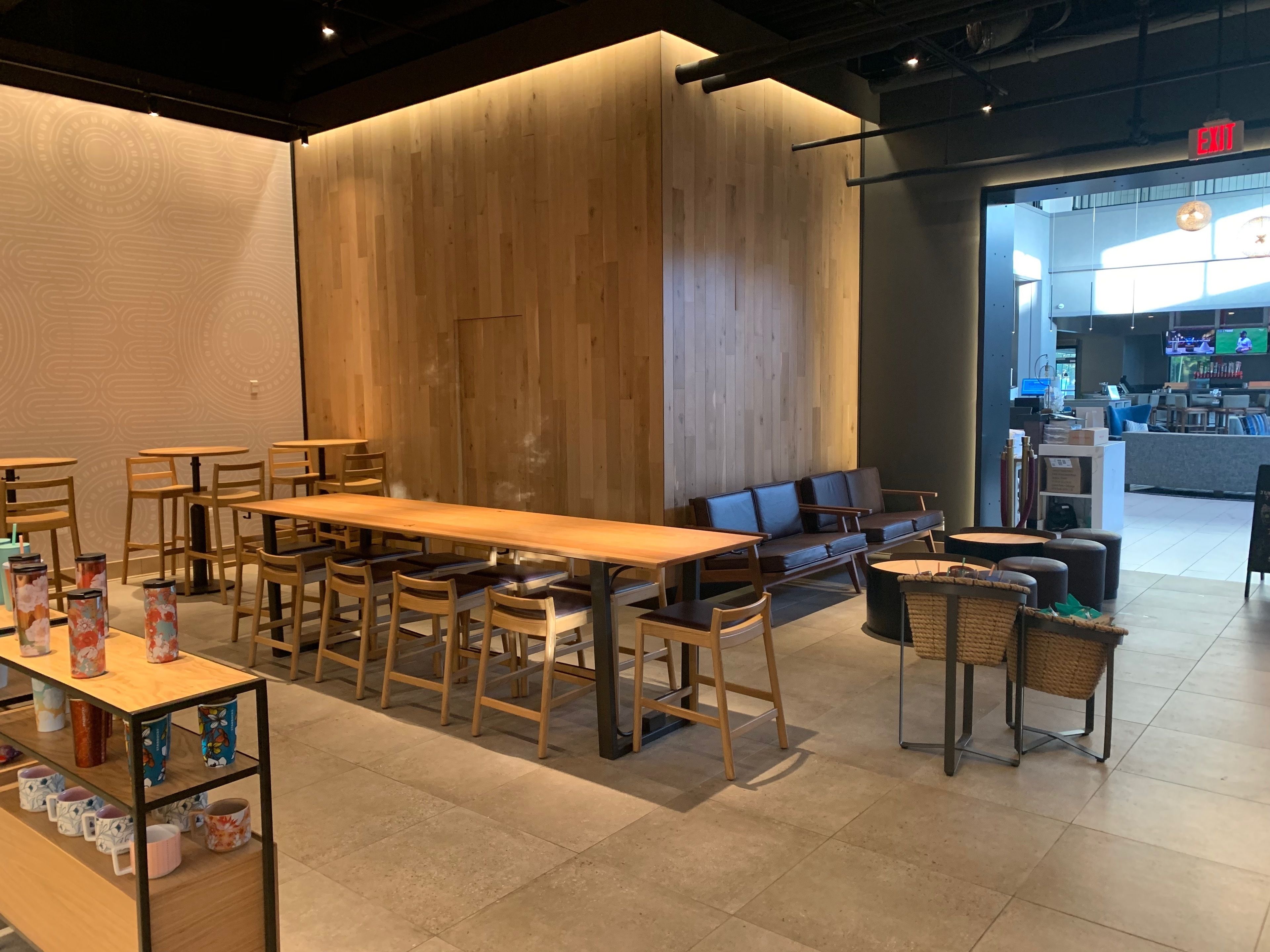 L’intérieur d’un café moderne est agrémenté de tables et de chaises en bois, d’une longue table conviviale et d’un espace détente avec un canapé et des poufs.