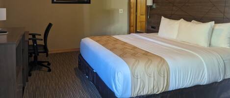 A hotel room with a bed, a desk, and a chair. There is a painting on the wall and a wooden headboard.