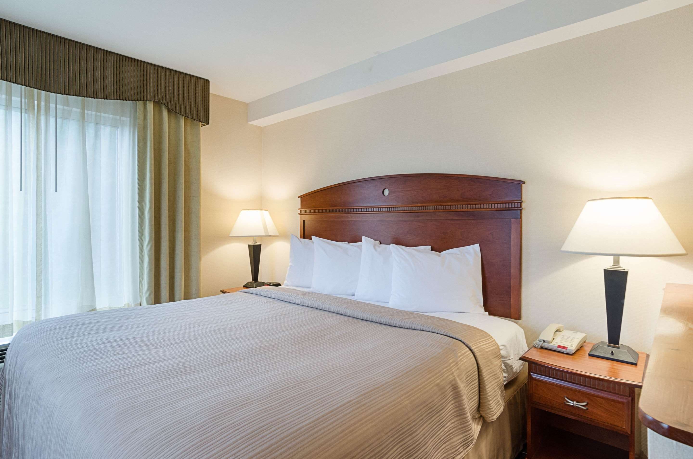 A hotel room with a large bed, two bedside tables with lamps, a nightstand, and a window with curtains.