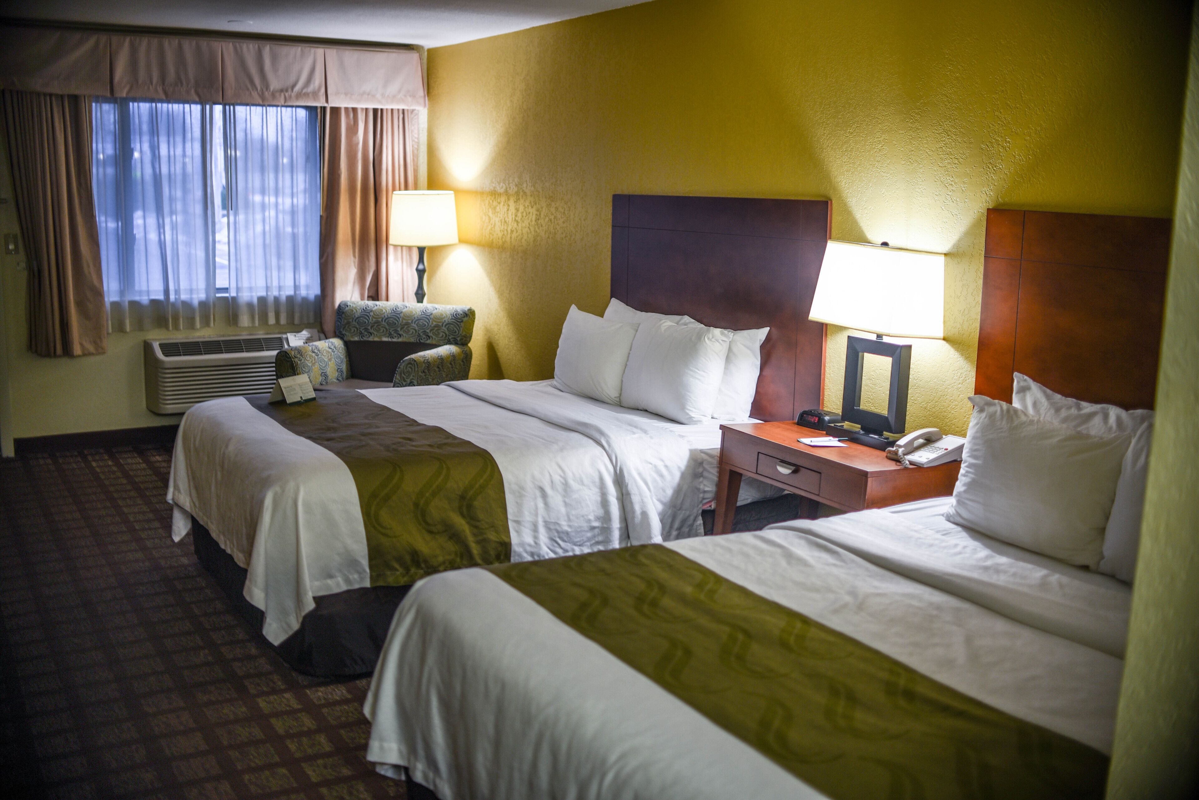 A hotel room with two beds, a desk, a chair, a lamp, and a telephone.