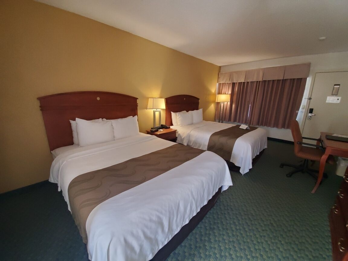 A hotel room with two beds, a desk, and a chair.