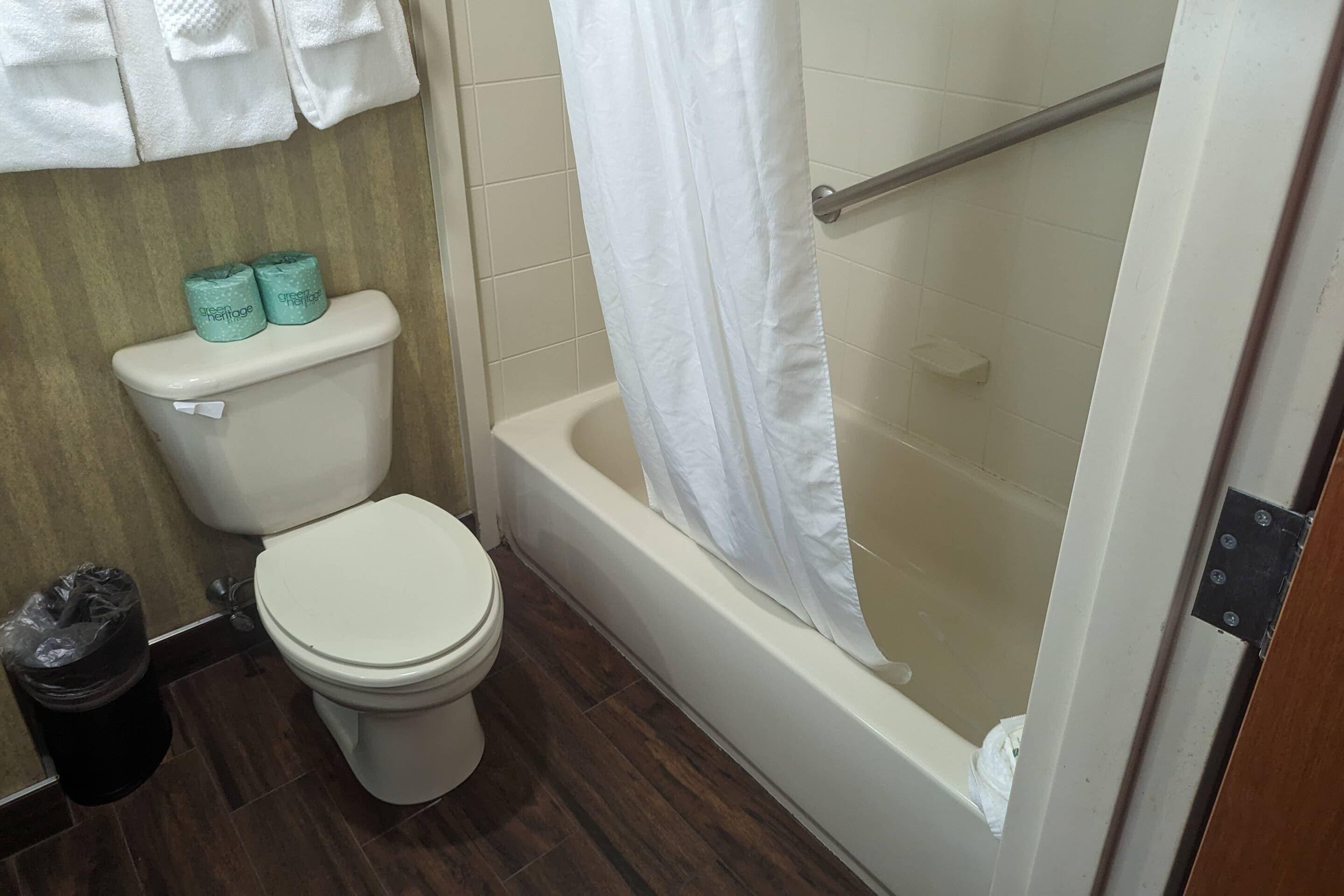 A bathroom with a toilet, a bathtub with a shower curtain, and two rolls of toilet paper on the toilet tank.