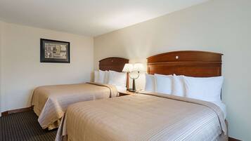 A hotel room with two beds, a nightstand with lamps, a framed picture on the wall, and a carpeted floor.