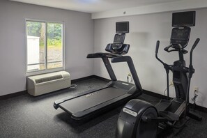 A gym with treadmills, an elliptical, and a stationary bike. There is a window with a view of trees and a white air conditioning unit.