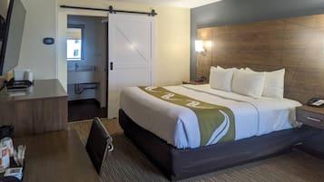 A hotel room with a bed, bedside table, desk, chair, and a bathroom visible through an open door.