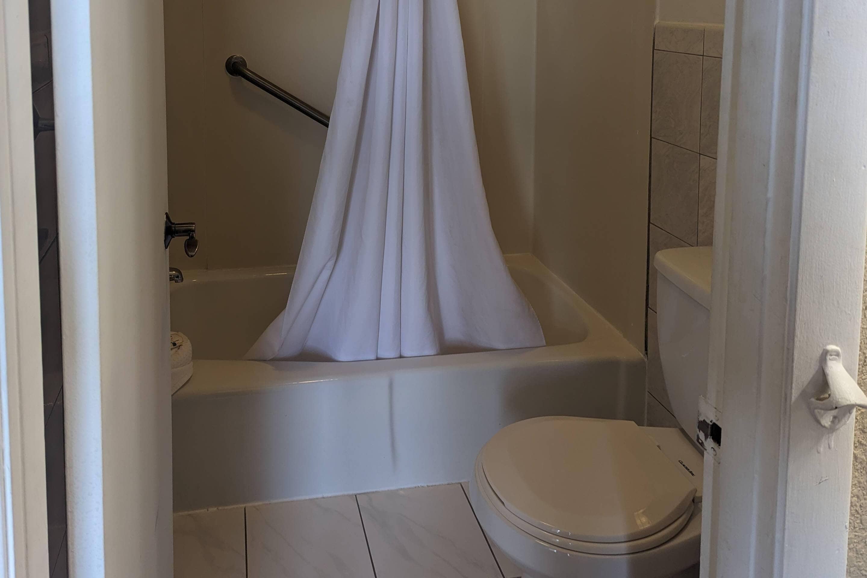 Et badeværelse med badekar, toilet og bruseforhæng.