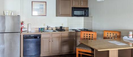 A compact kitchen with a refrigerator, dishwasher, microwave, and a small dining area with a chair.