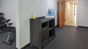 Un pasillo con una cinta de correr, un dispensador de agua y una puerta que da a otra habitación.