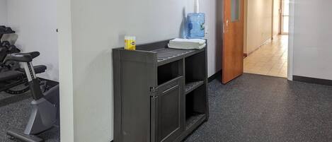 A hallway with a treadmill, a water dispenser, and a door leading to another room.