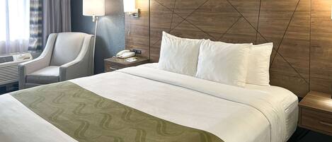 Habitación de hotel con una cama grande, una silla, una mesita de noche con lámpara y un teléfono en la pared.