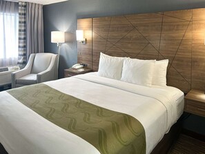 A hotel room with a large bed, a chair, a nightstand with a lamp, and a wall-mounted phone.