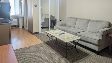 A living room with a sofa, a coffee table, a TV, and a kitchen area with a refrigerator and sink.