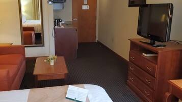 A hotel room with a bed, a desk, a television, a mirror, and a kitchenette.