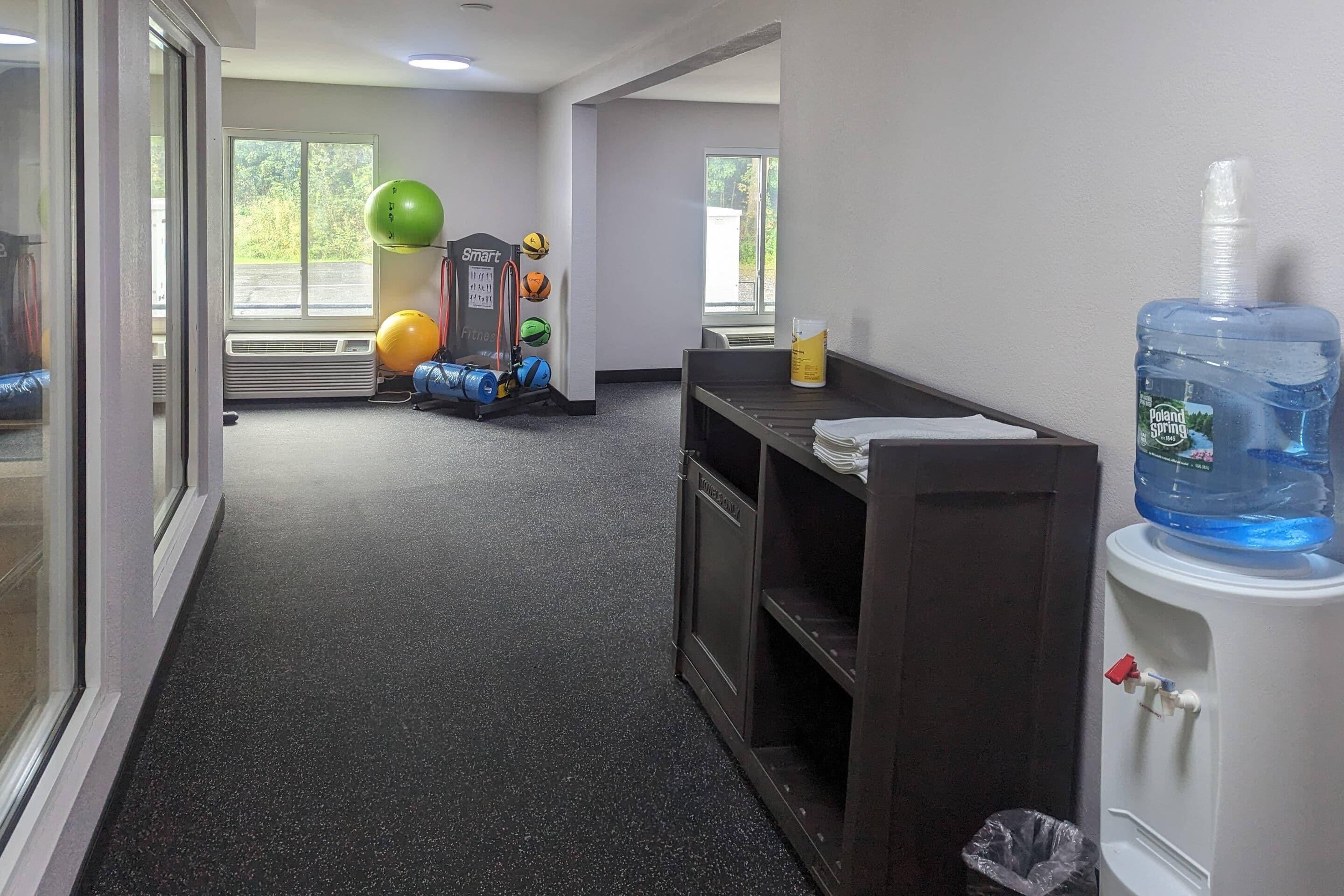 Corredor com bebedouro, bolas de exercício e janela com vista para vegetação.