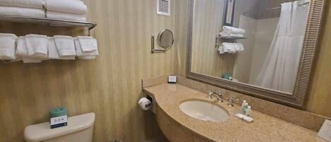 A bathroom with a toilet, sink, and mirror. There are towels on a rack and a trash can.