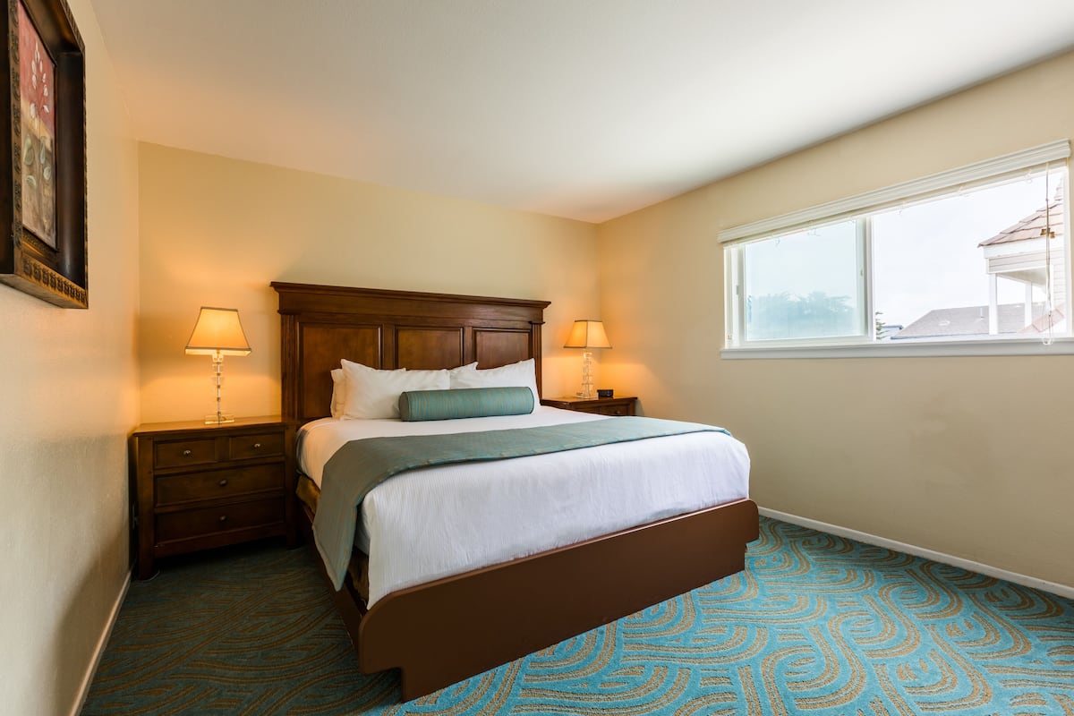 A neatly made bed with a wooden headboard, two bedside tables with lamps, and a window with a view of a building.