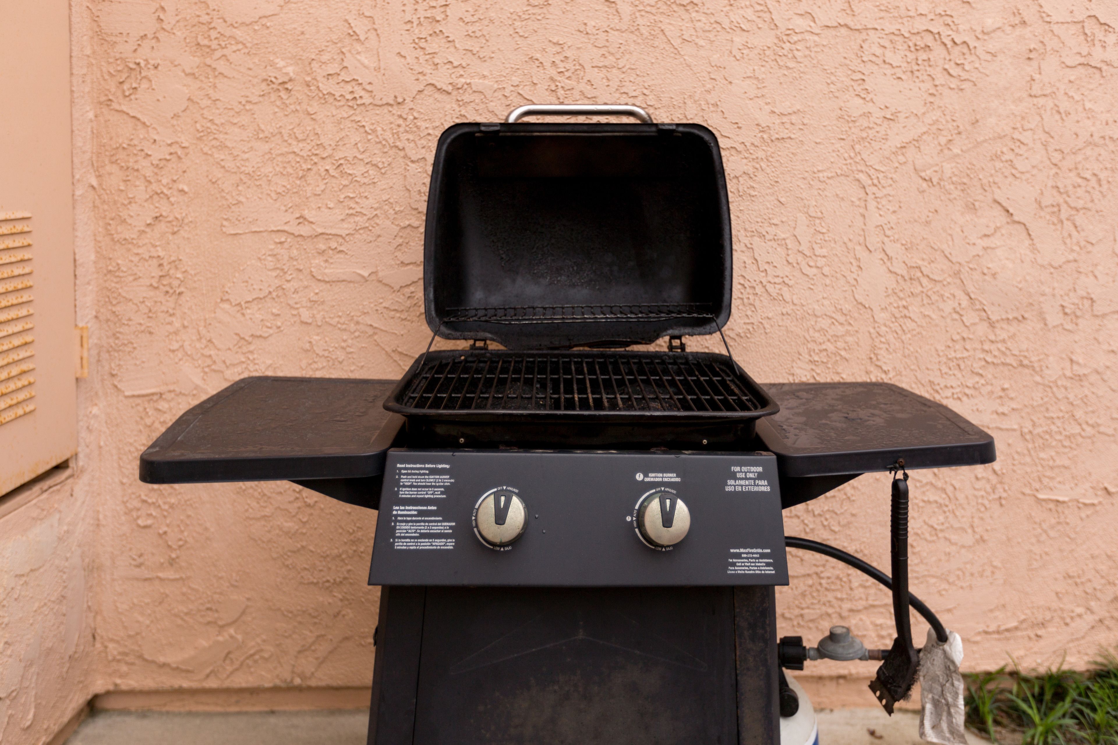 Ein tragbarer Grill mit zwei Drehknöpfen und einer seitlichen Ablagefläche vor einer strukturierten Wand.