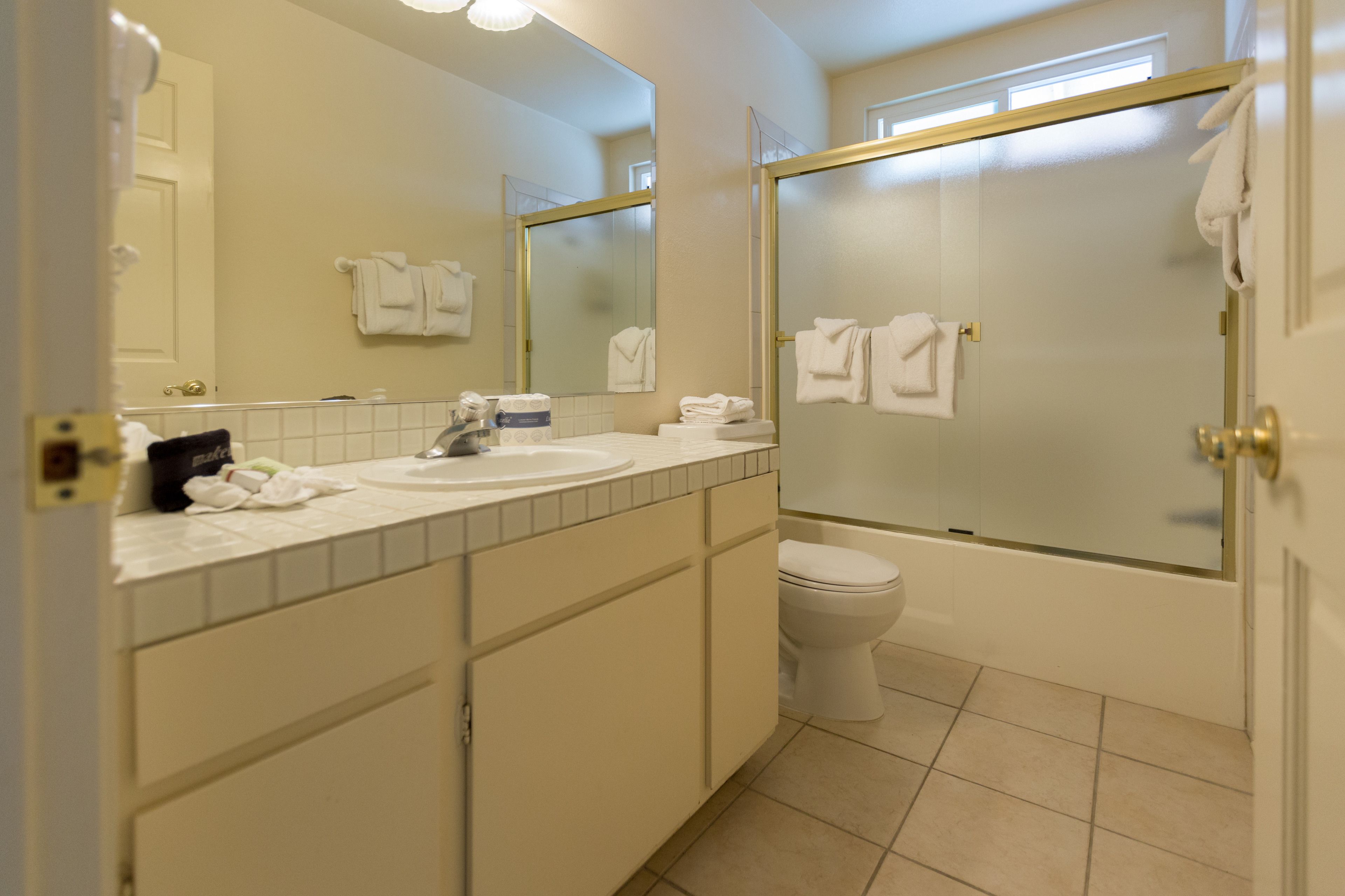 A bathroom with a toilet, sink, and mirror. There are towels hanging on the wall and a shower area.
