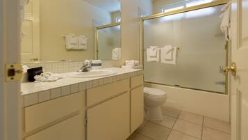 A bathroom with a toilet, sink, and mirror. There are towels hanging on the wall and a shower area.