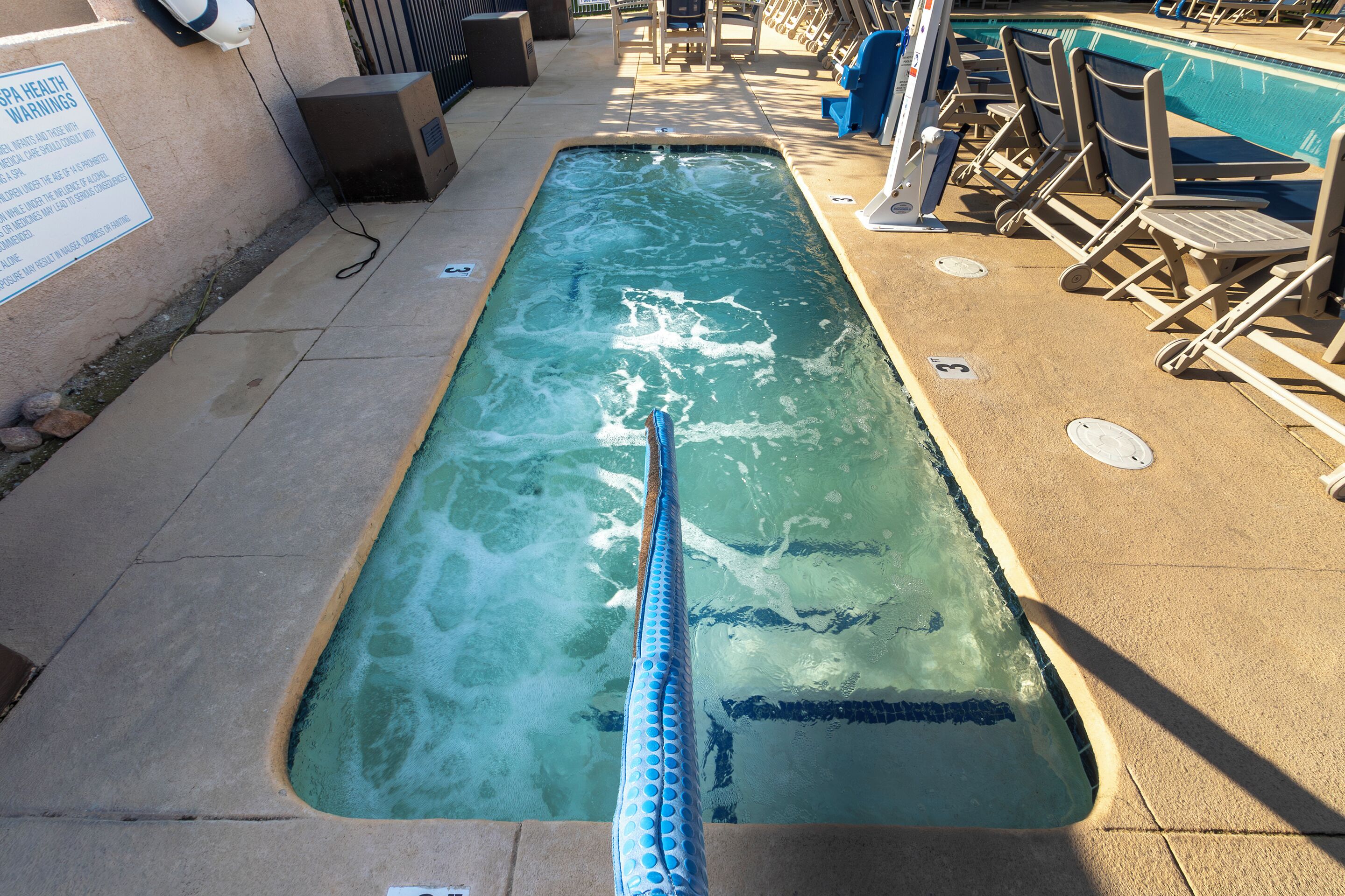 Une piscine dotée de séparateurs de couloirs, de chaises longues et d’un panneau affiché sur le mur.