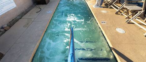 A swimming pool with a lane divider, lounge chairs, and a sign on the wall.