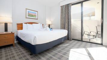 A hotel room with a bed, a nightstand, a lamp, a painting, and a view through a glass door to an outdoor area.