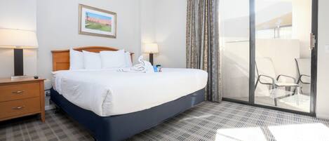 Habitación de hotel con cama, mesita de noche, lámpara, un cuadro y vistas al exterior a través de un ventanal.