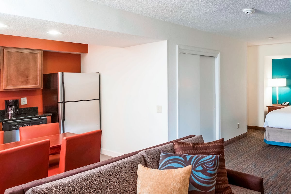 A hotel room with a kitchenette, a bed with a TV, and a view of the hallway.