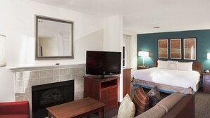 A hotel room with a fireplace, a television, a bed with two pillows, a nightstand with a lamp, and a wall with three framed pictures.