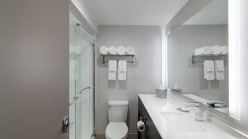 A modern bathroom with a glass shower enclosure, a toilet, a sink with a mirror, and towel racks.