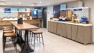 A modern cafe with a wooden counter, bar stools, and a variety of food and drink dispensers.
