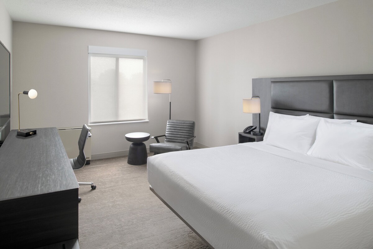 Une chambre d’hôtel avec un grand lit, un bureau, une chaise, une lampe et une fenêtre.