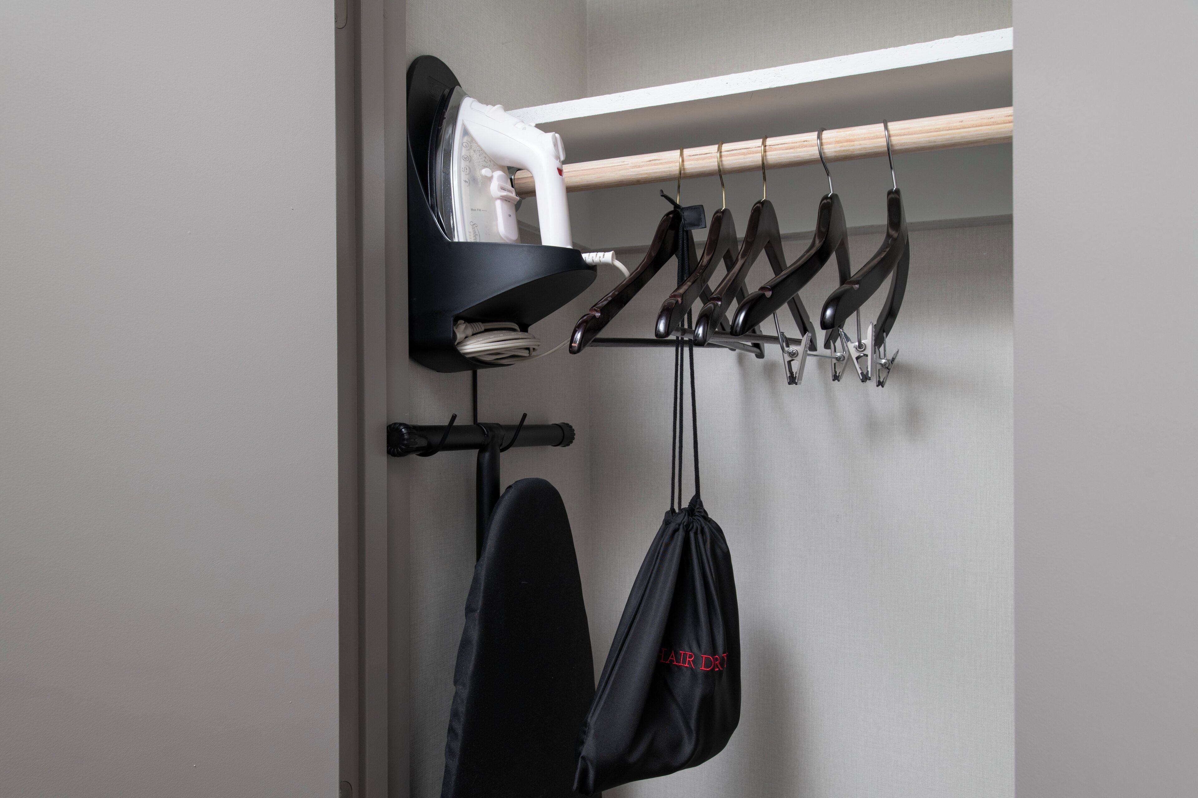 Una tabla de planchar fijada a la pared, con un implemento para planchar y un perchero con varias planchas.