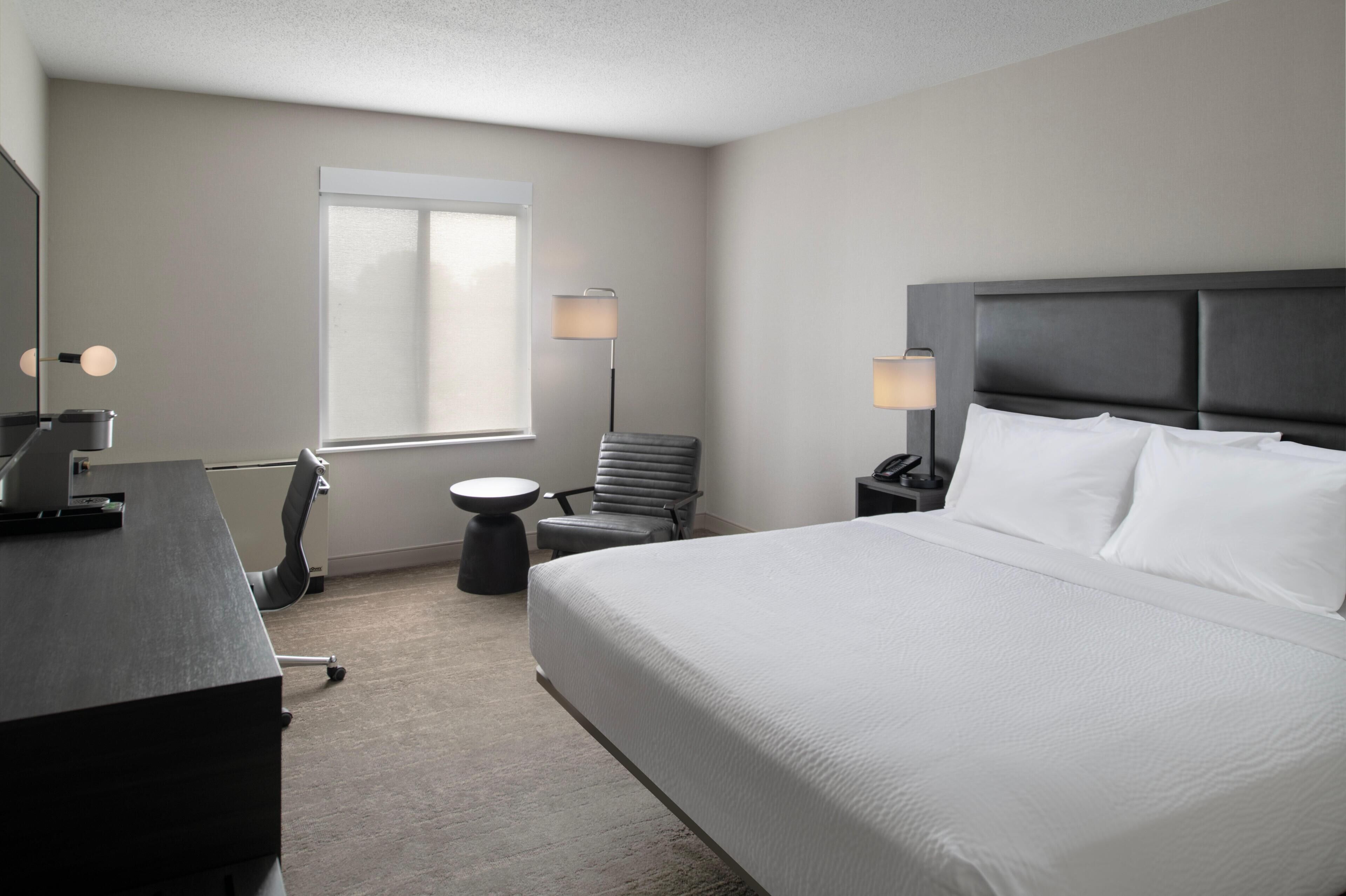 A hotel room with a bed, desk, chair, lamp, and a window.
