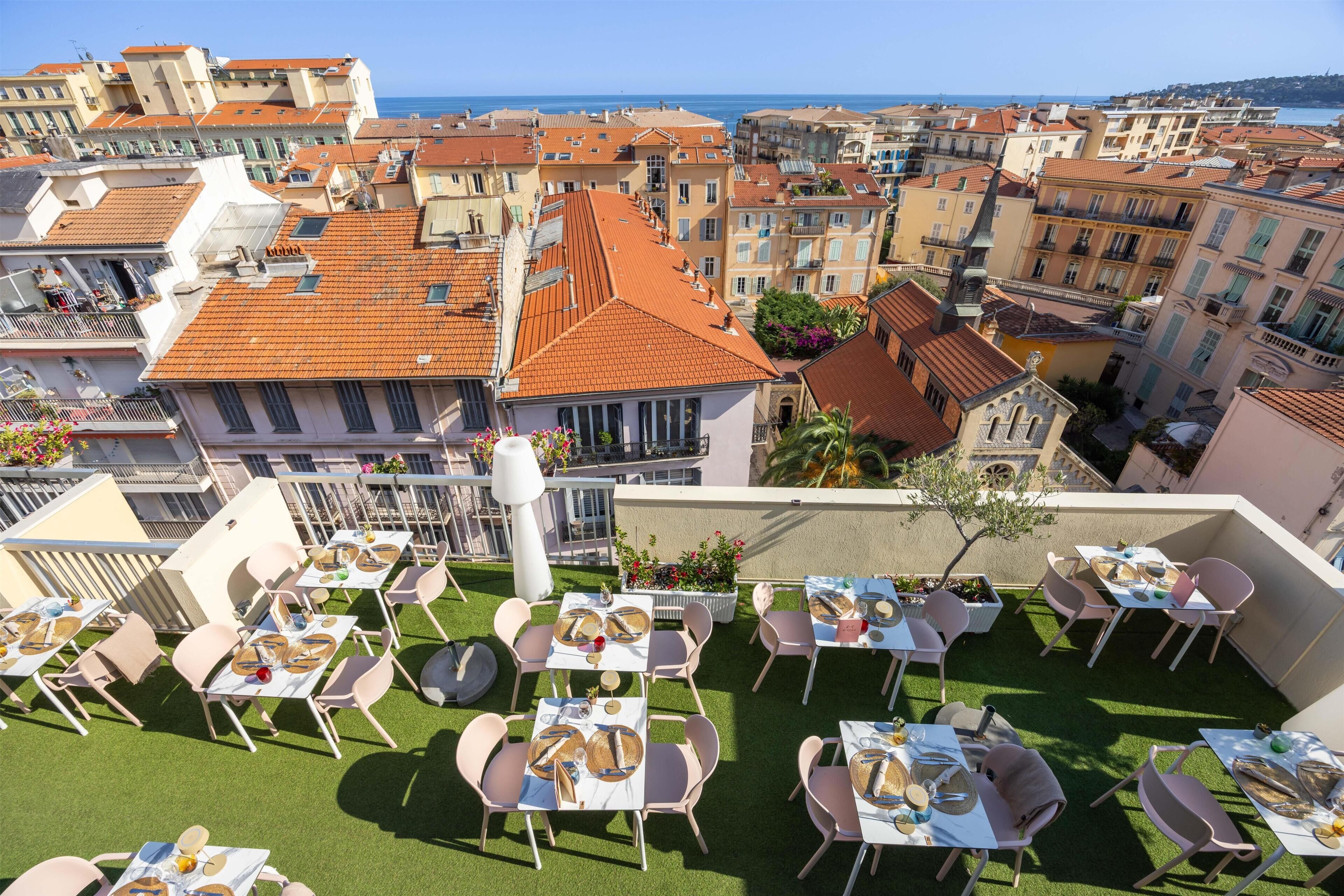 A rooftop terrace with tables and chairs, overlooking a coastal cityscape.