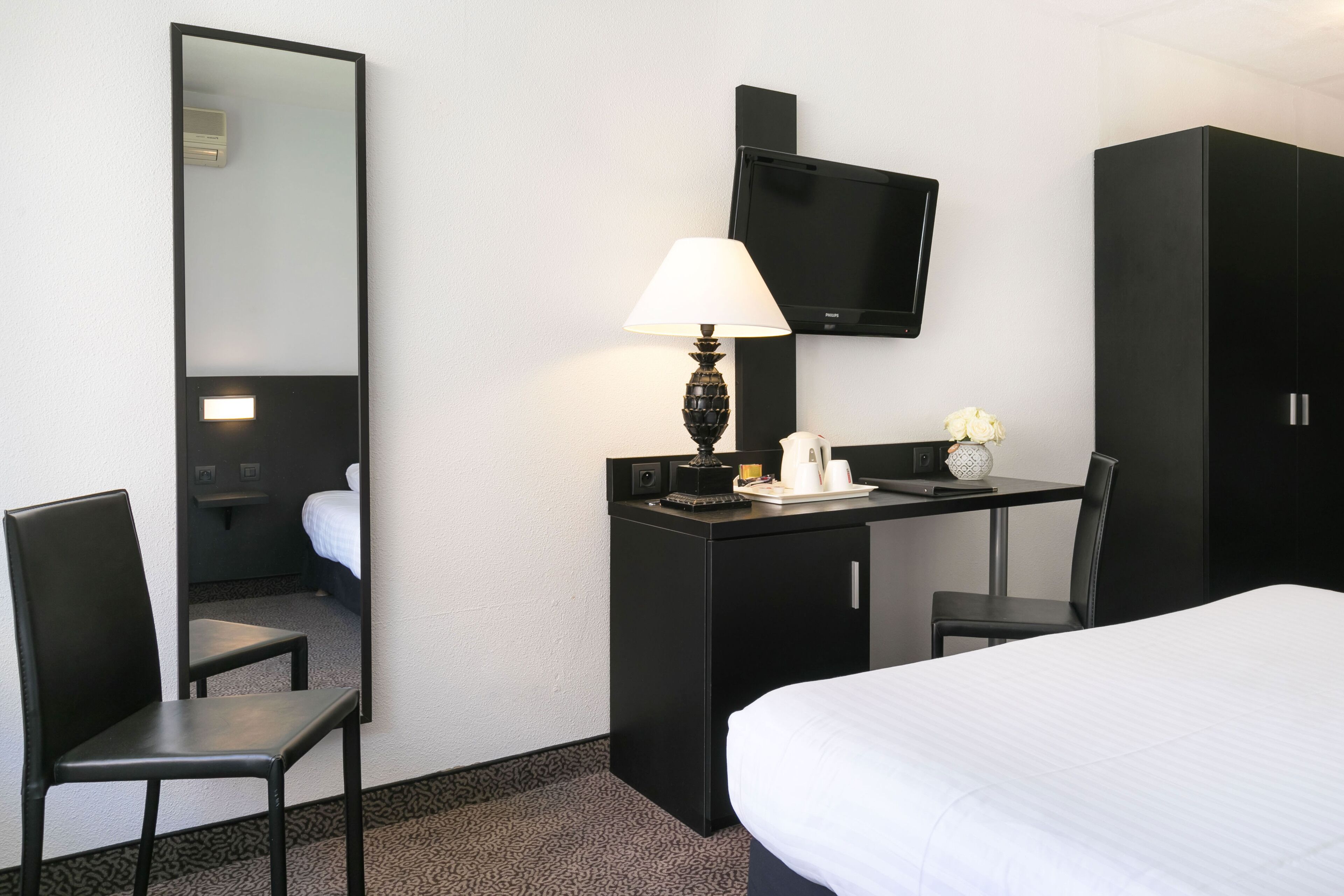 Habitació d'hotel amb un llit, una taula de treball amb una làmpada, una televisió i un mirall.