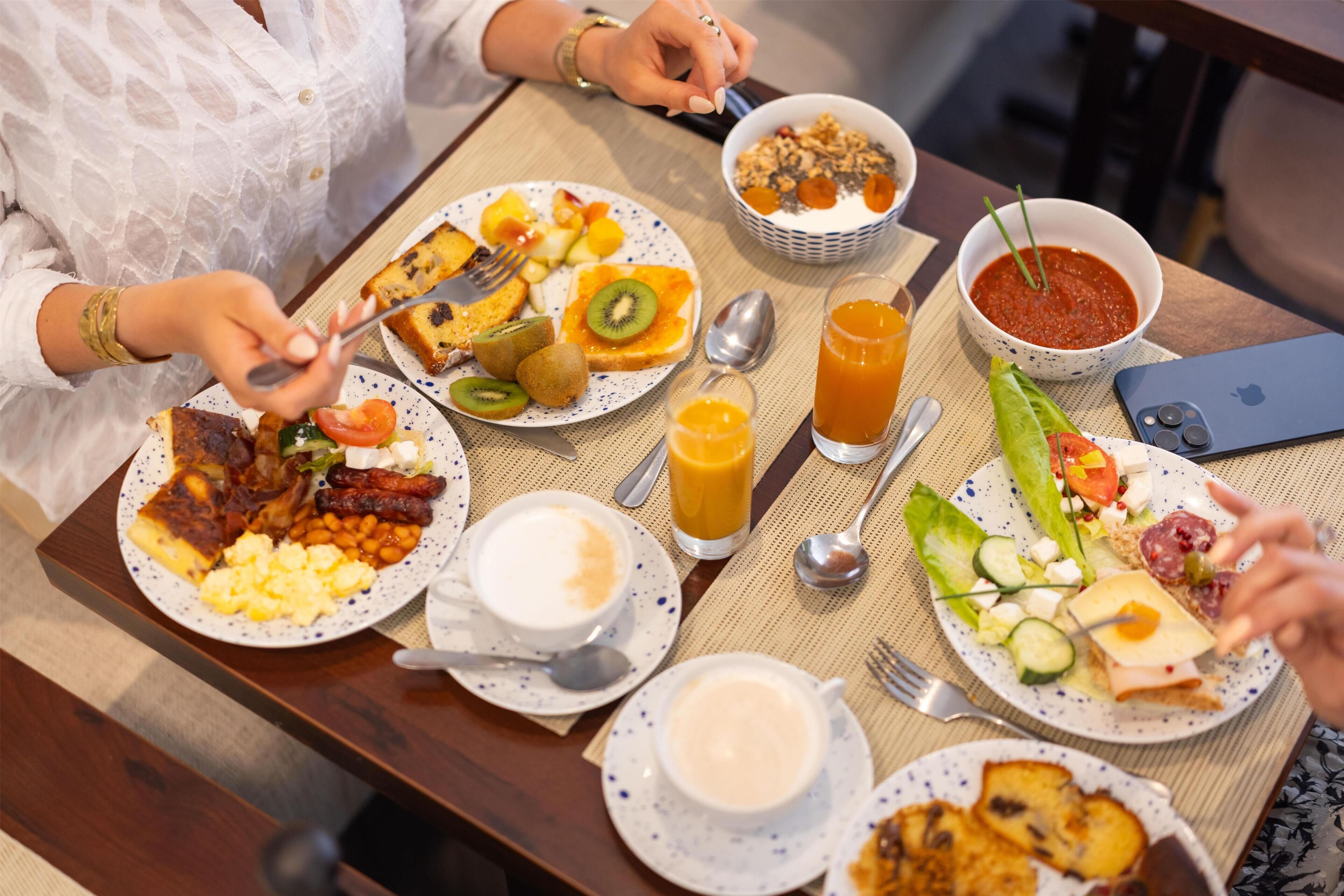 A breakfast setting with various dishes, a smartphone, and a tablet on the table.